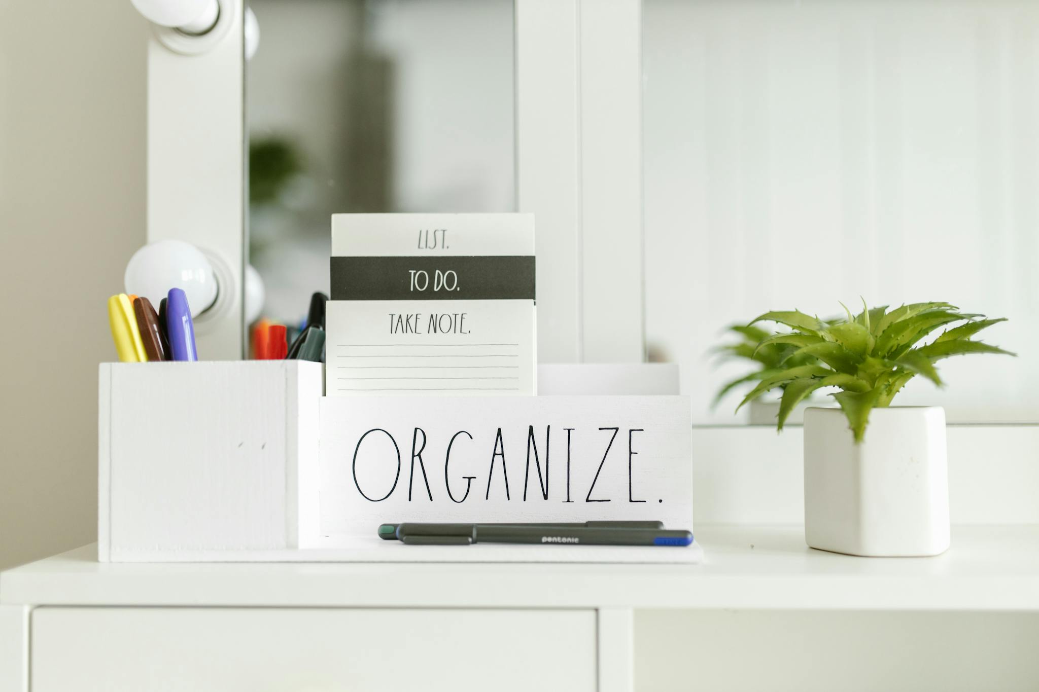 Close-up of an organized workspace featuring a notebook, pen holder, and green plant.